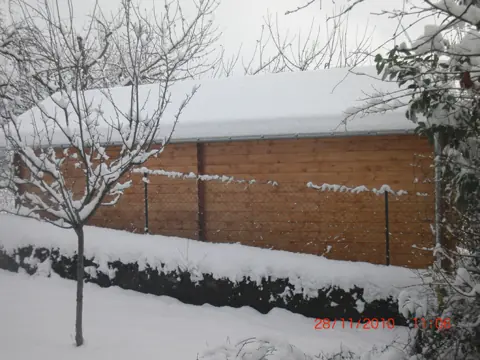 Garage en madriers enneigé, haie au premier plan