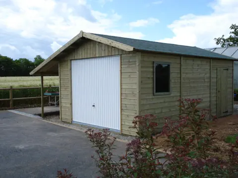 Garage bois lasuré vert avec auvent latéral, massif fleuri