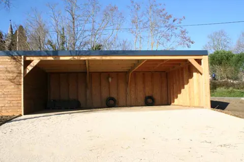 Carport accolé à un garage toit plat, sol sablé