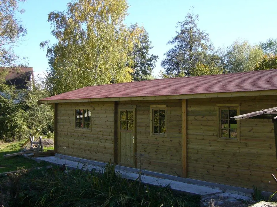 Long garage en madriers, bardeaux rouges, jardin