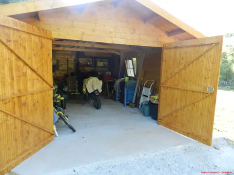 Garage en madriers, portes ouvertes, intérieur rempli
