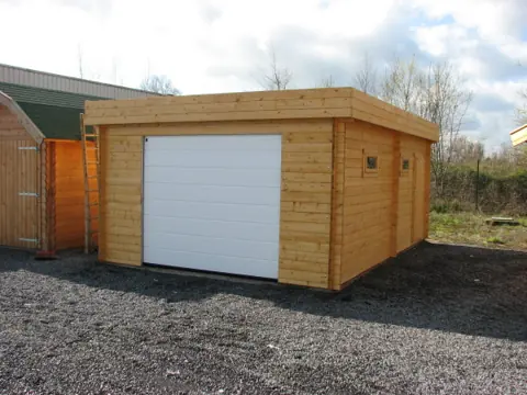 Garage toit plat en madriers, porte sectionnelle blanche