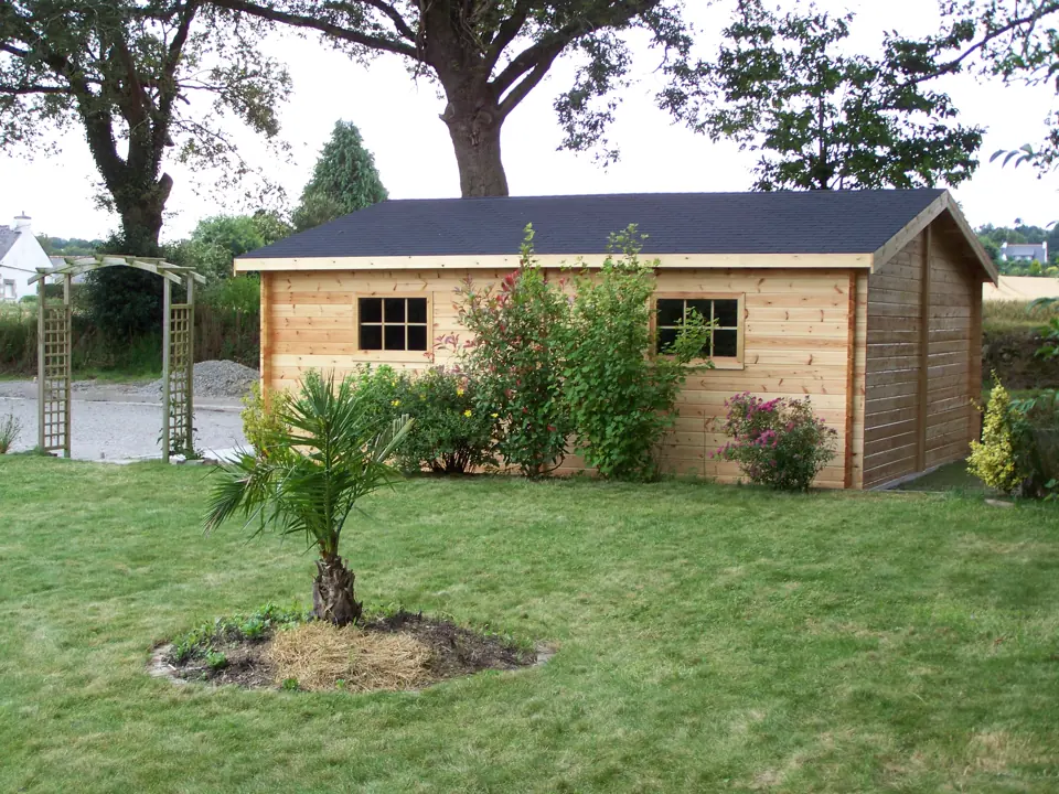 Garage en madriers, toit bardeaux, palmier devant